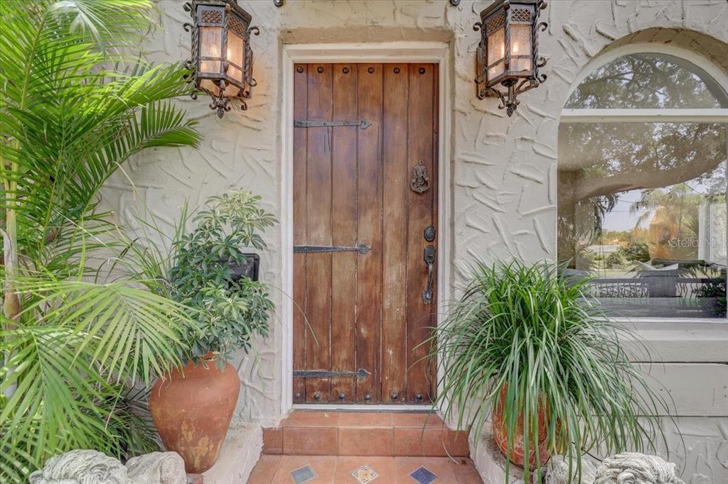 A wooden arched-top door with iron hinges sits between two lanterns and potted plants — 325 49TH STREET N, ST PETERSBURG, FL