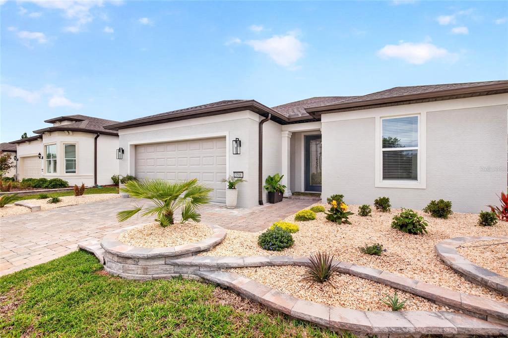 A single-story house exterior features a beige stucco facade, a two-car garage, and landscaped rock beds — 8866 SW 57TH PLACE ROAD, OCALA, FL