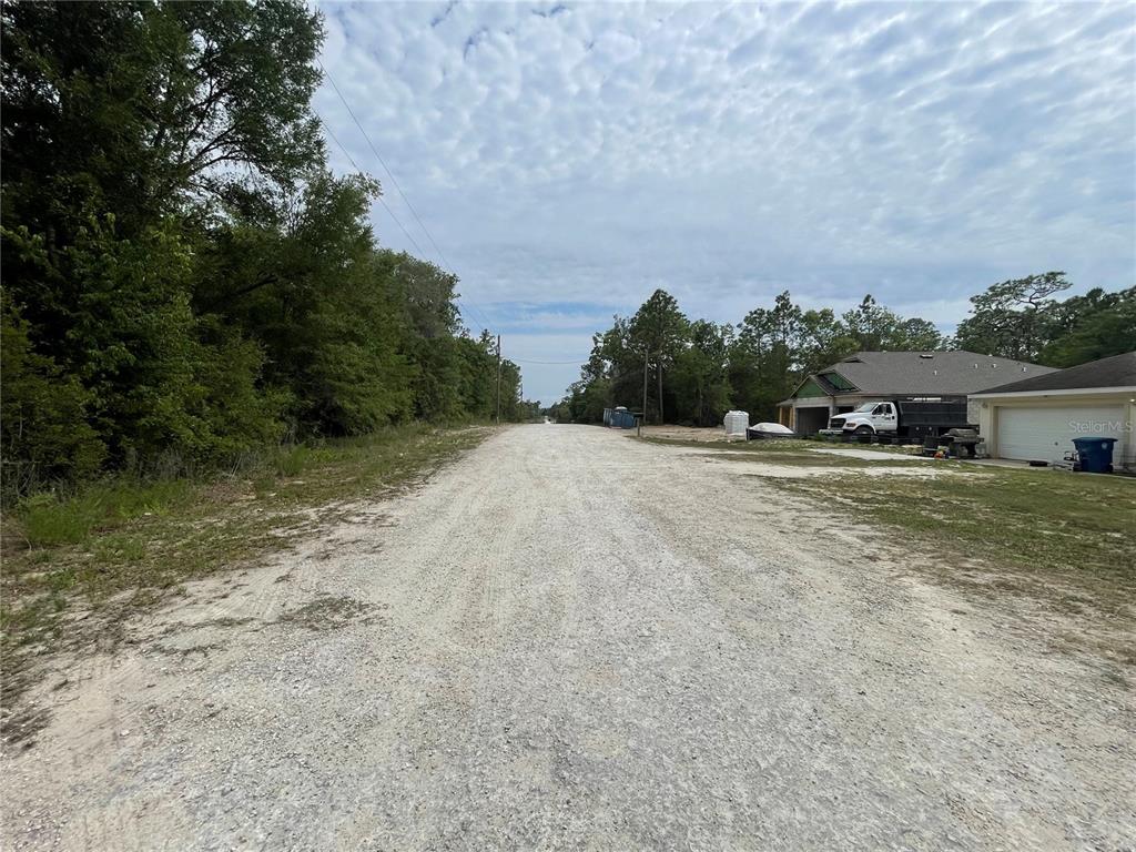 A gravel road leads past a wooded area and a house under construction — 16486 CURLEW ROAD, BROOKSVILLE, FL