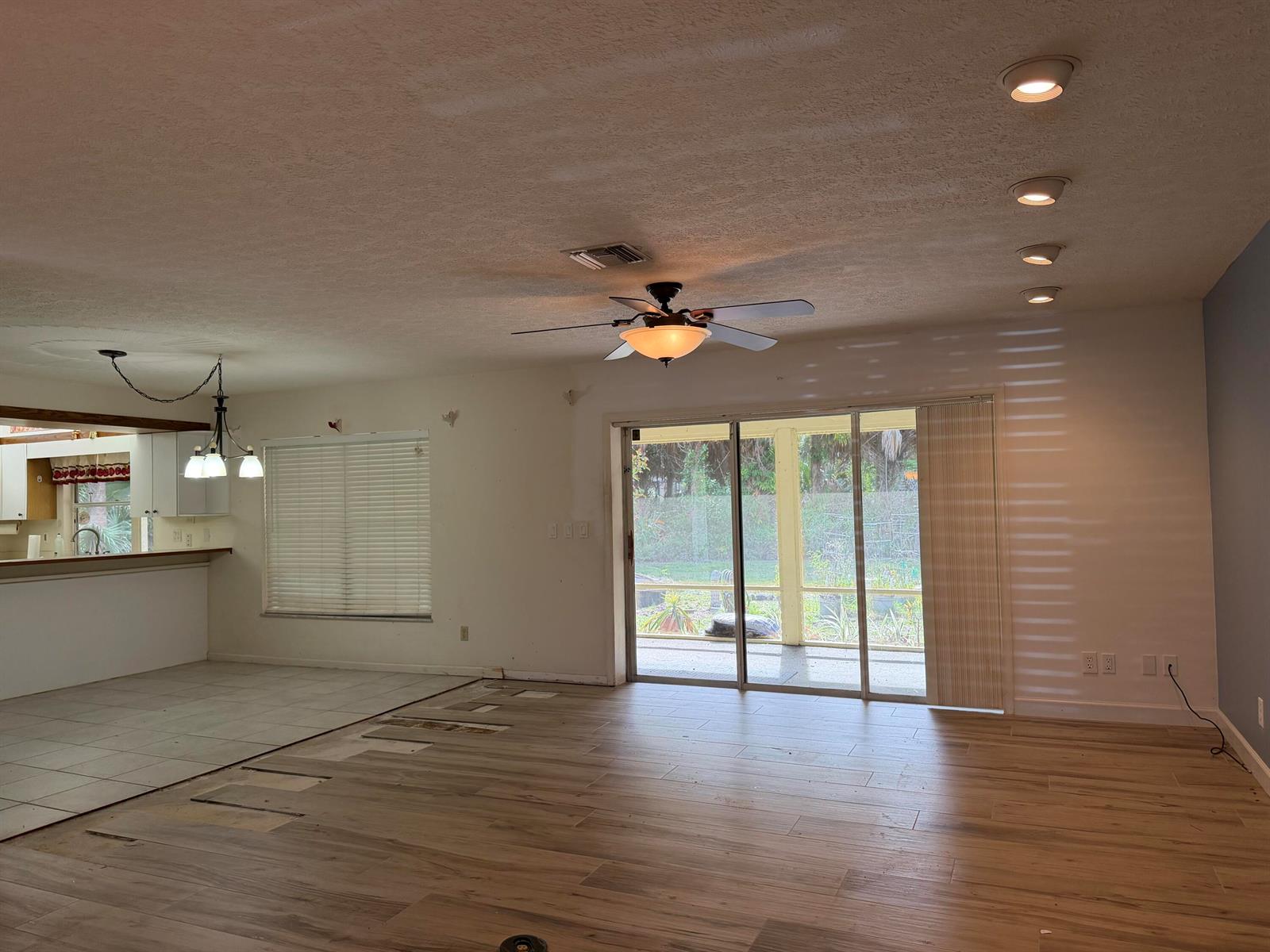 An open-concept living area features wood-look tile flooring, a ceiling fan, and sliding glass doors — 1140 SE Buttonwood Circle, Stuart FL 34997, STUART, FL