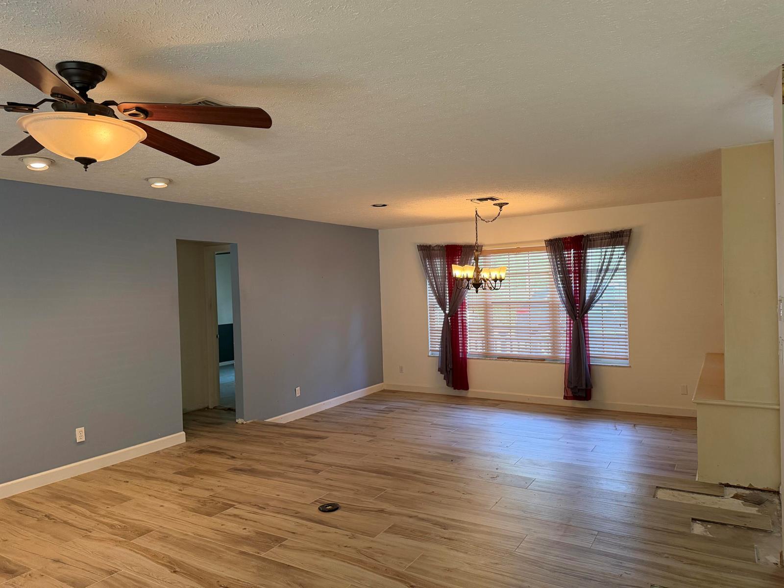 A spacious living room features wood-look tile flooring, a ceiling fan, and a dining chandelier — 1140 SE Buttonwood Circle, Stuart FL 34997, STUART, FL