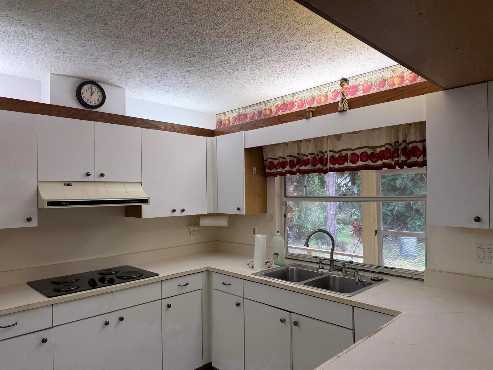 A kitchen features white cabinets, a black cooktop, a double sink, and apple-themed wallpaper border — 1140 SE Buttonwood Circle, Stuart FL 34997, STUART, FL