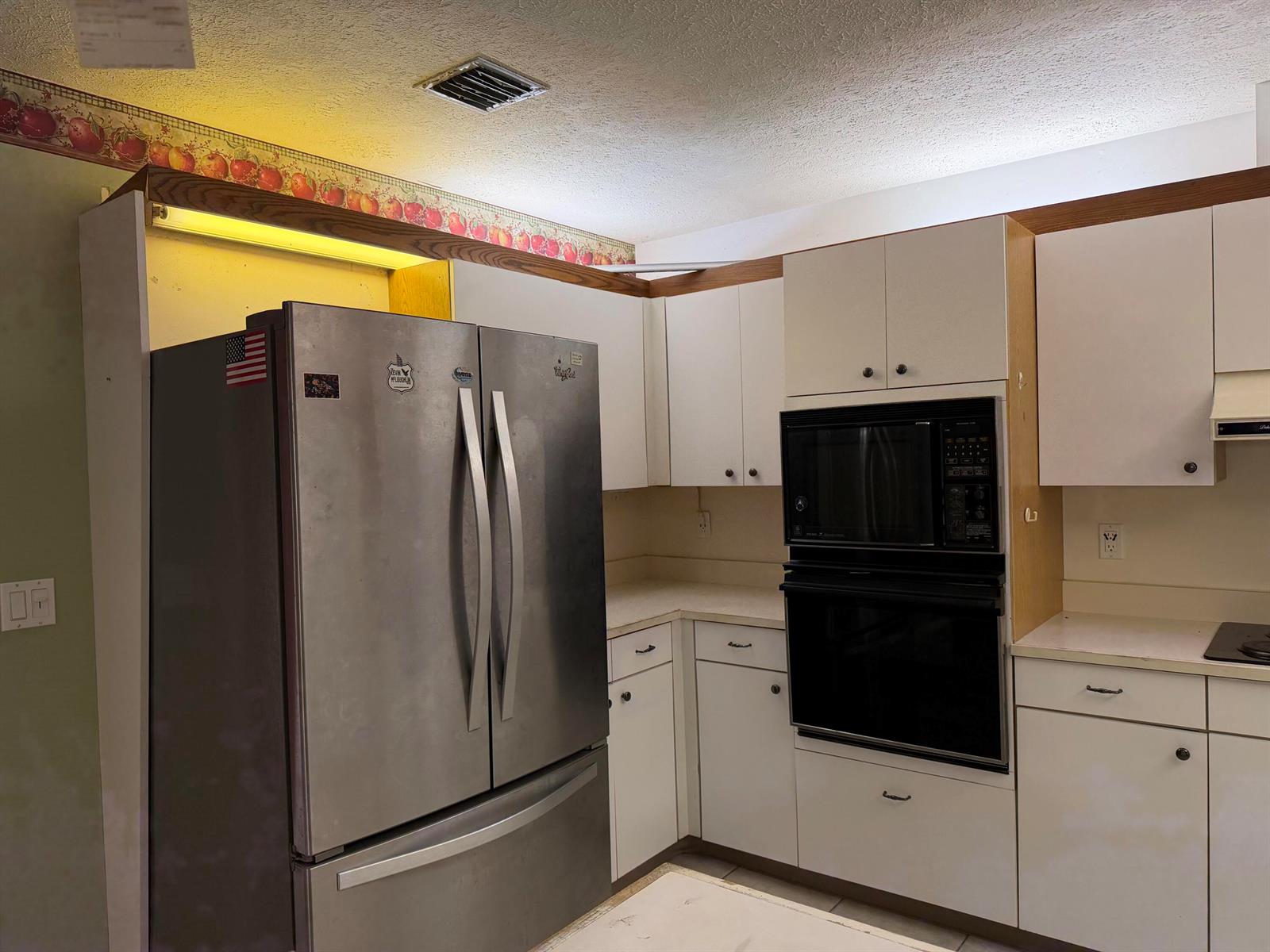 A kitchen features white cabinets, stainless steel appliances, and a decorative fruit-patterned wallpaper border — 1140 SE Buttonwood Circle, Stuart FL 34997, STUART, FL