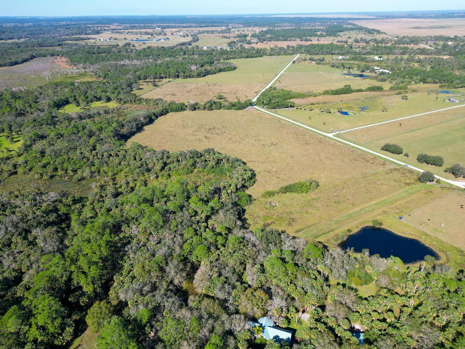 An aerial view shows a house nestled in trees next to open fields and ponds — 3702 SW Wild Turkey Lane, Okeechobee FL 34974, OKEECHOBEE, FL