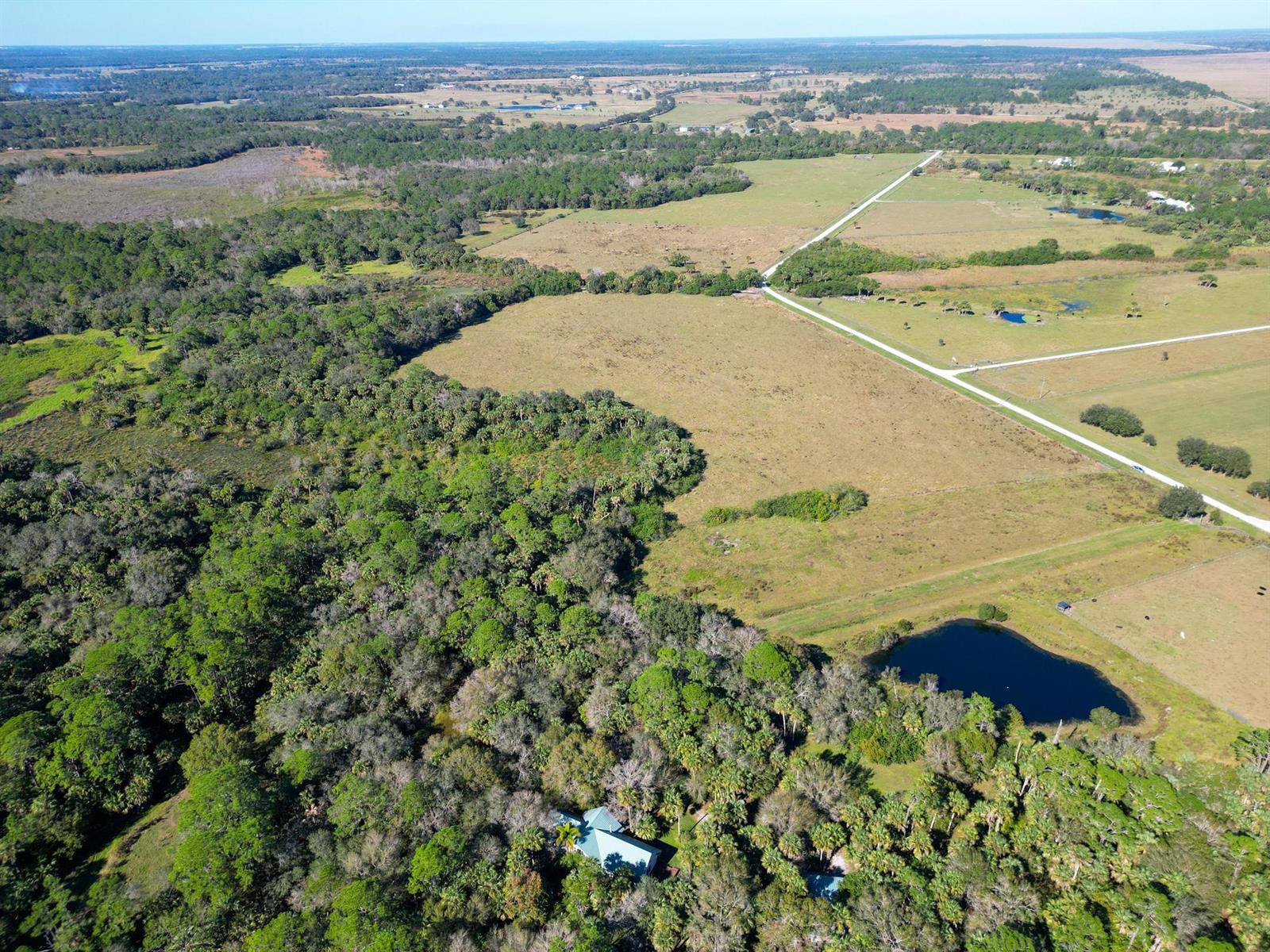 An aerial view shows a house nestled in a forest next to a large pond — 3702 SW Wild Turkey Lane, Okeechobee FL 34974, OKEECHOBEE, FL