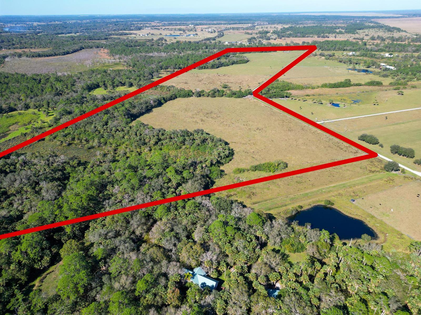 An aerial view shows a large, open grassy field outlined in red near a pond — 3702 SW Wild Turkey Lane, Okeechobee FL 34974, OKEECHOBEE, FL