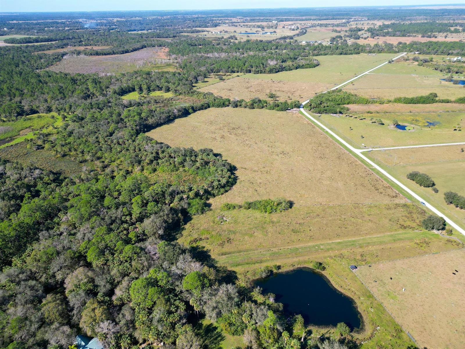 An aerial view shows a large pasture, a small pond, and surrounding wooded areas — 3702 SW Wild Turkey Lane, Okeechobee FL 34974, OKEECHOBEE, FL