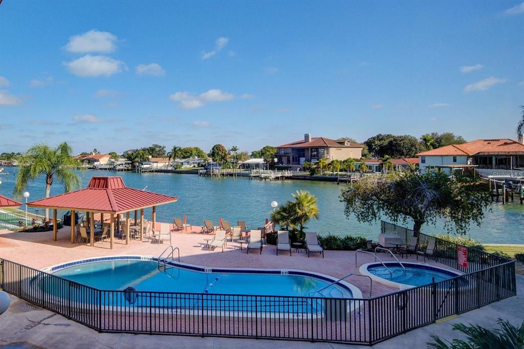 A swimming pool and hot tub overlook a canal with a gazebo and lounge chairs — 105 ISLAND WAY UNIT 132, CLEARWATER, FL