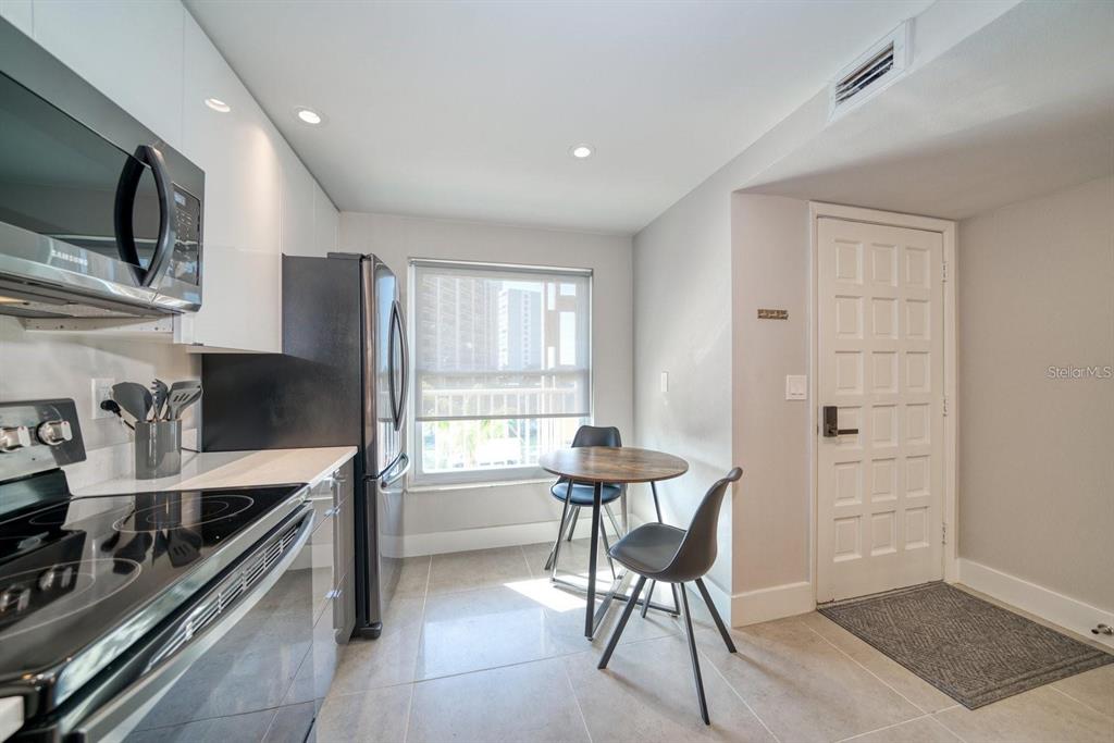 A modern kitchen features white cabinets, stainless steel appliances, and a small dining table — 105 ISLAND WAY UNIT 132, CLEARWATER, FL