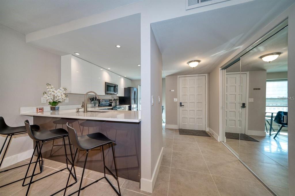 A kitchen with a breakfast bar and stools overlooks a tiled entryway with a front door — 105 ISLAND WAY UNIT 132, CLEARWATER, FL