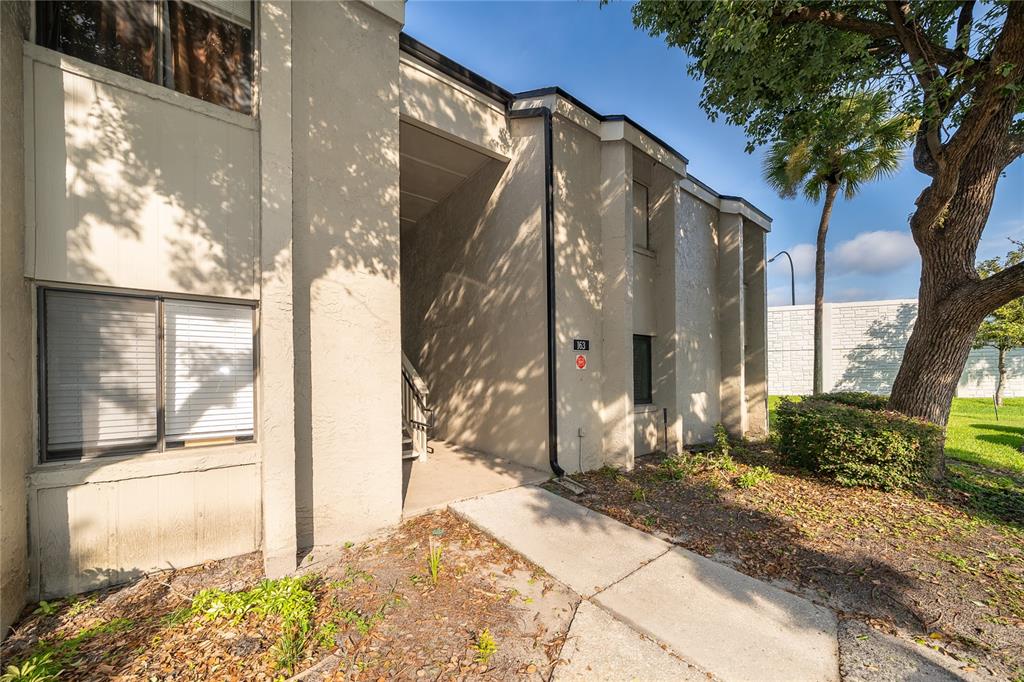 The exterior of a beige multi-story apartment building features a covered entryway and a sidewalk — 163 SPRINGWOOD CIRCLE UNIT B, LONGWOOD, FL