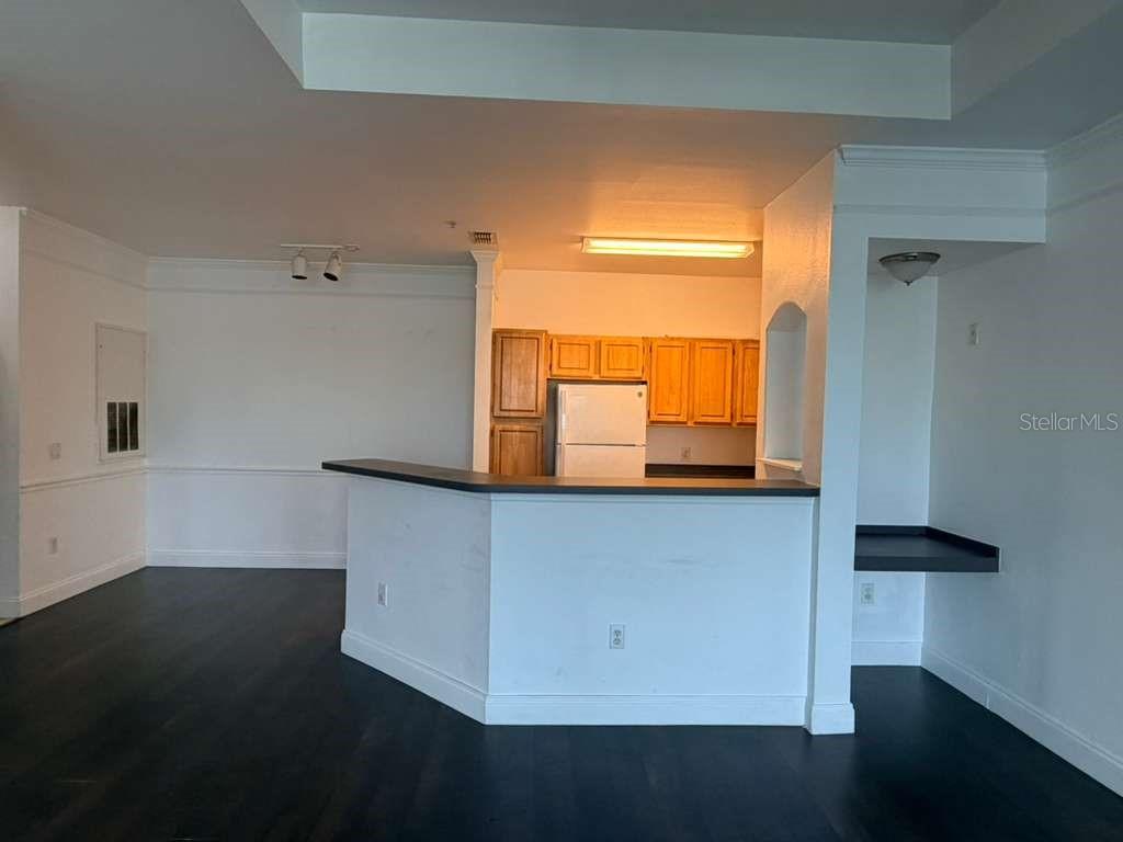 A kitchen with wooden cabinets and a breakfast bar overlooks an empty living area — 6413 ASTOR VILLAGE AVENUE UNIT 303, ORLANDO, FL