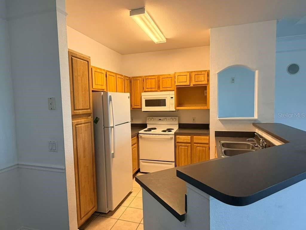 A kitchen features light wood cabinets, white appliances, and a black countertop breakfast bar — 6413 ASTOR VILLAGE AVENUE UNIT 303, ORLANDO, FL