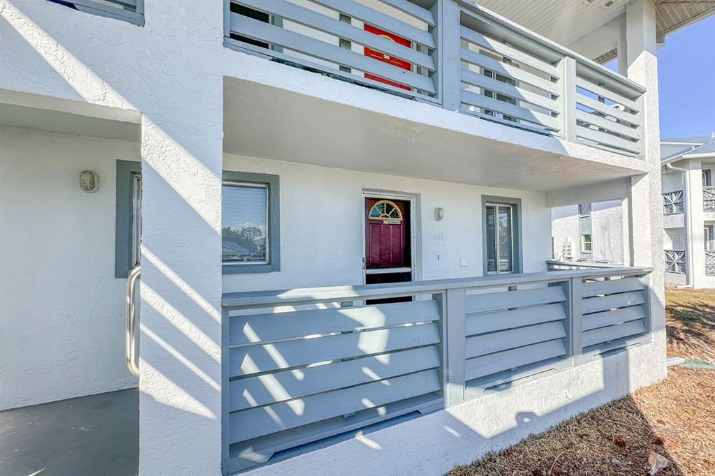 A two-story building exterior features white stucco walls, grey horizontal railings, and a red door — 6800 PLACIDA ROAD UNIT 169, ENGLEWOOD, FL