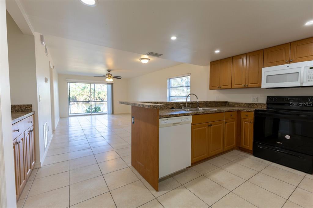 A kitchen with wood cabinets and tile floors opens into a living area with sliding doors — 6800 PLACIDA ROAD UNIT 169, ENGLEWOOD, FL