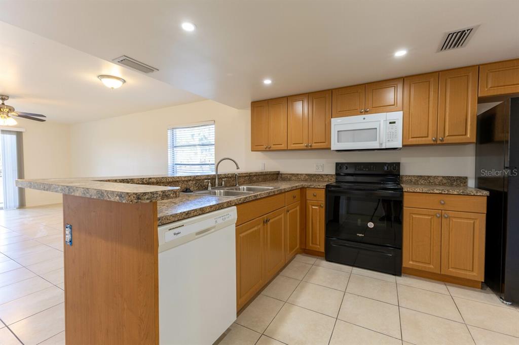 A kitchen features wood cabinets, granite countertops, a white dishwasher, and black appliances — 6800 PLACIDA ROAD UNIT 169, ENGLEWOOD, FL