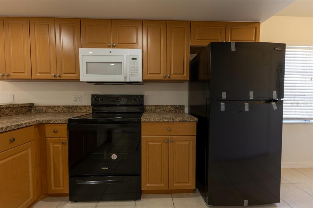 A kitchen features wooden cabinets, granite countertops, and black appliances with a white microwave — 6800 PLACIDA ROAD UNIT 169, ENGLEWOOD, FL