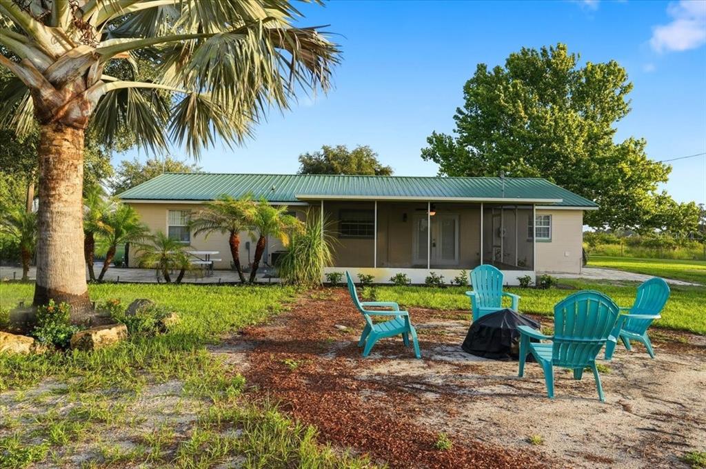 A single-story house with a green metal roof features a screened porch and fire pit — 1645 HWY 630 W, FROSTPROOF, FL