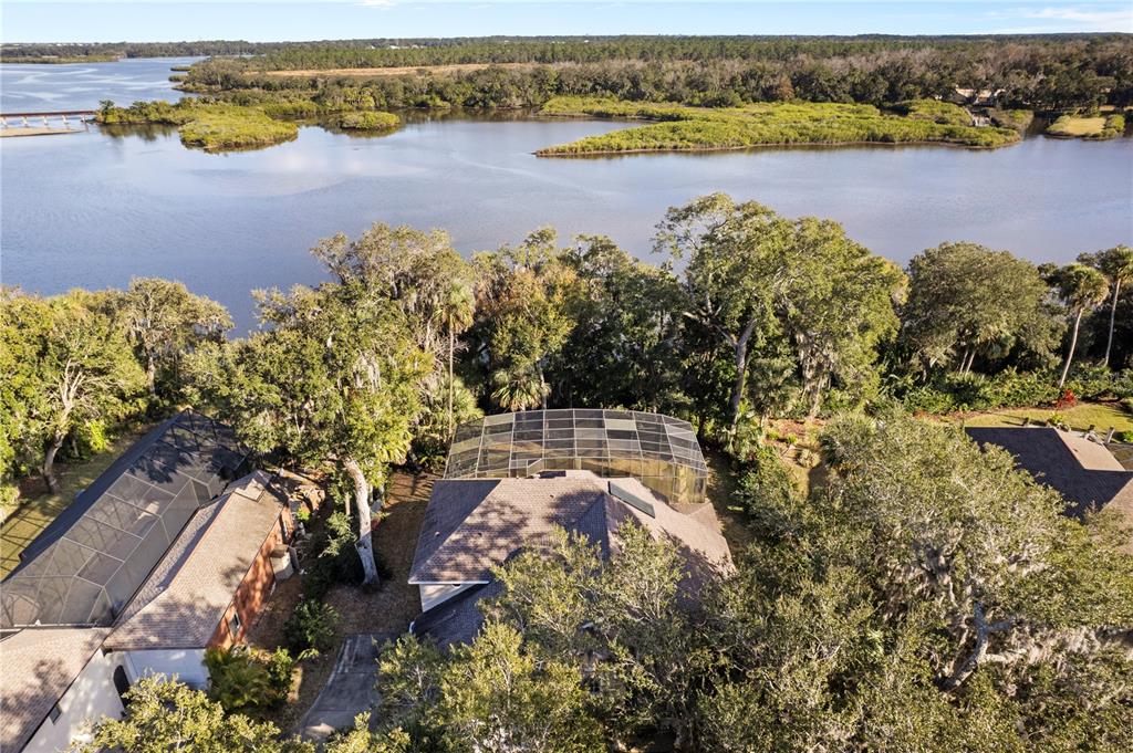 An aerial view shows a house with a screened pool enclosure near a large river — 6311 PALMAS BAY CIRCLE, PORT ORANGE, FL
