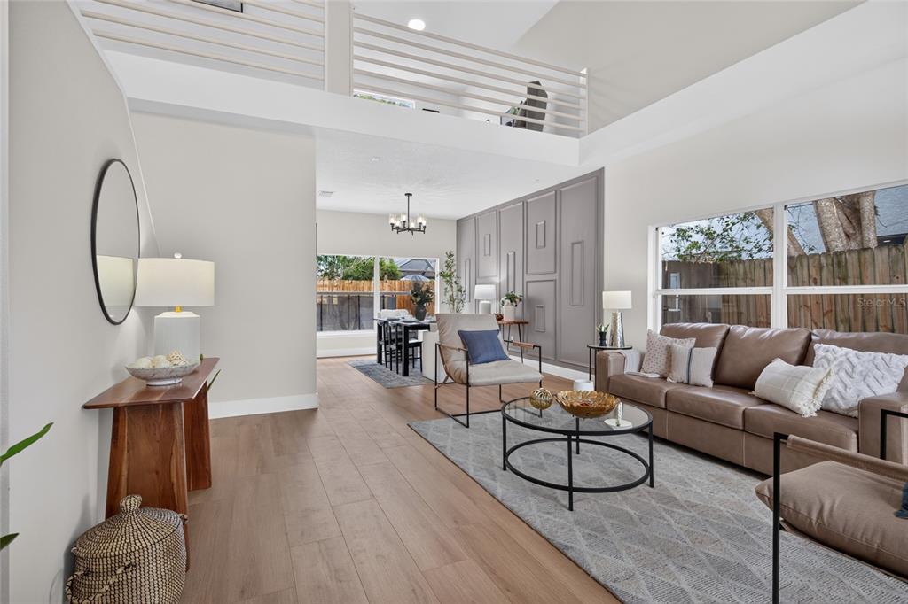 A bright living room features light wood flooring, a gray accent wall, and a lofted balcony — 11328 CLAYRIDGE DRIVE, TAMPA, FL