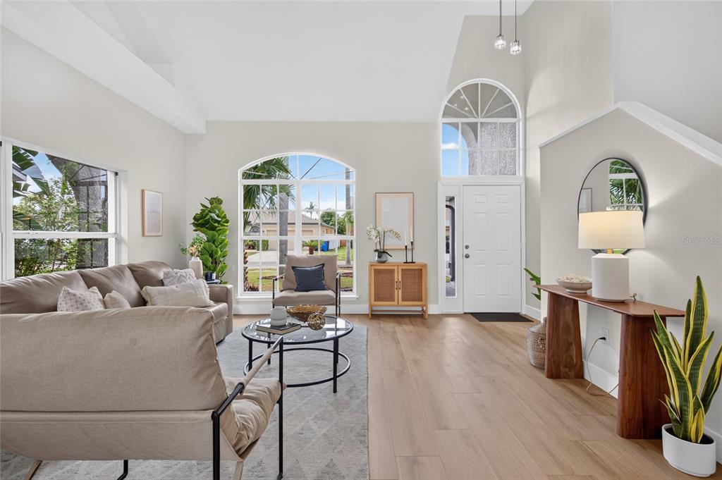 A bright living room features vaulted ceilings, light wood flooring, a sofa, and large windows — 11328 CLAYRIDGE DRIVE, TAMPA, FL