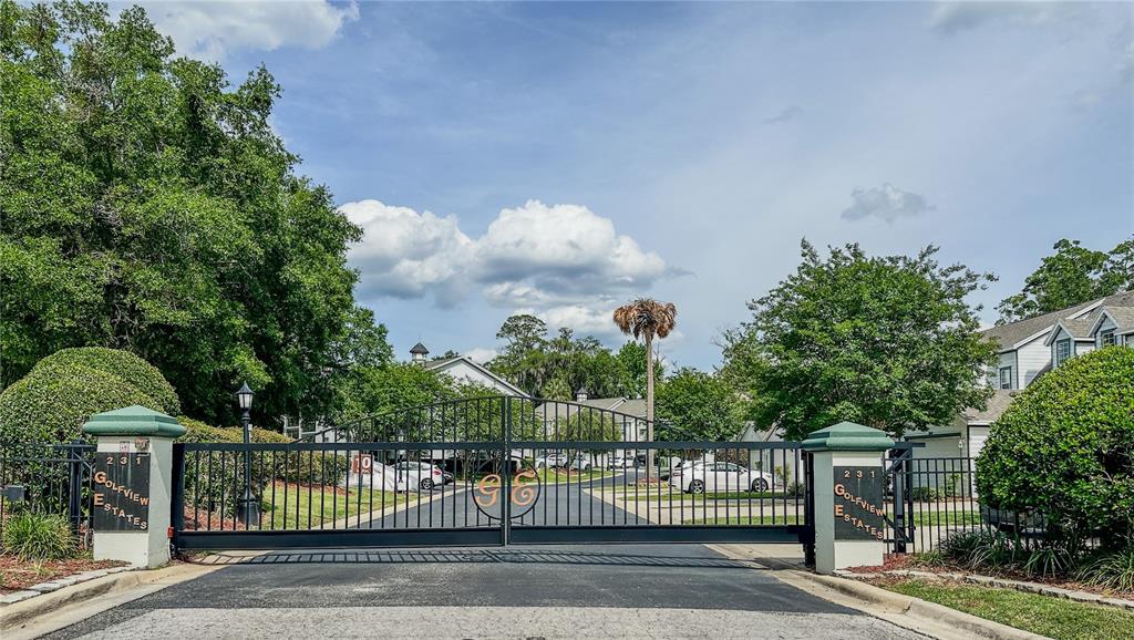 A black metal gate marks the entrance to a residential community with lush green trees — 231 NE 28TH AVENUE UNIT 308, OCALA, FL