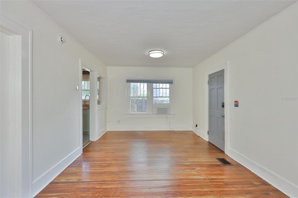 An empty room with hardwood floors, white walls, a window, and a gray door — 340 MOFFETT COURT N, ST PETERSBURG, FL