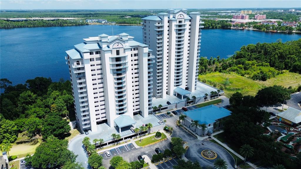 An aerial view shows two tall, light-colored residential towers situated beside a large lake — 13415 BLUE HERON BEACH DRIVE UNIT 109, ORLANDO, FL