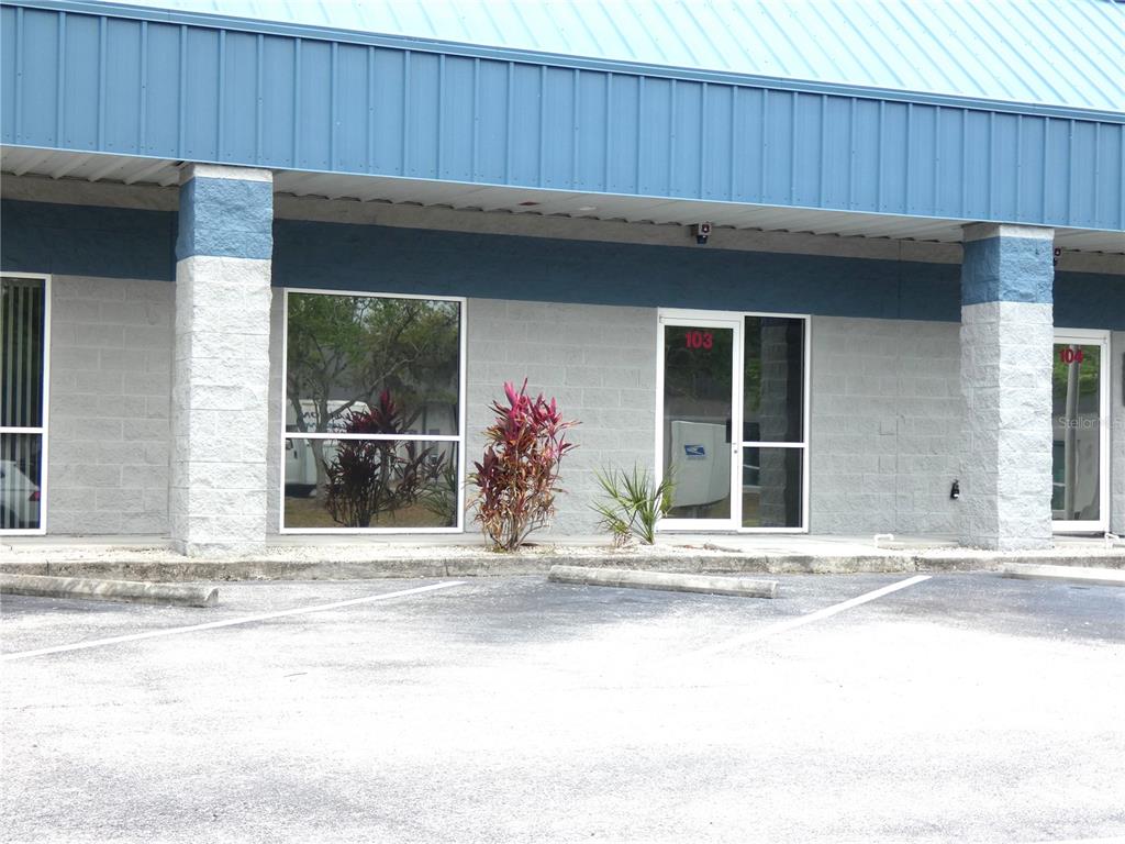 The exterior of a commercial building features gray concrete block walls, blue trim, and glass doors — 1882 PORTER LAKE DRIVE UNIT 103, SARASOTA, FL