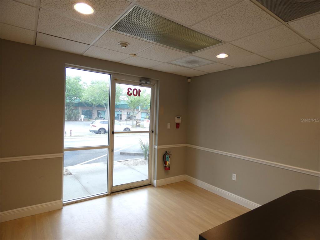 An office interior features light wood flooring, beige walls, a glass door, and ceiling tiles — 1882 PORTER LAKE DRIVE UNIT 103, SARASOTA, FL