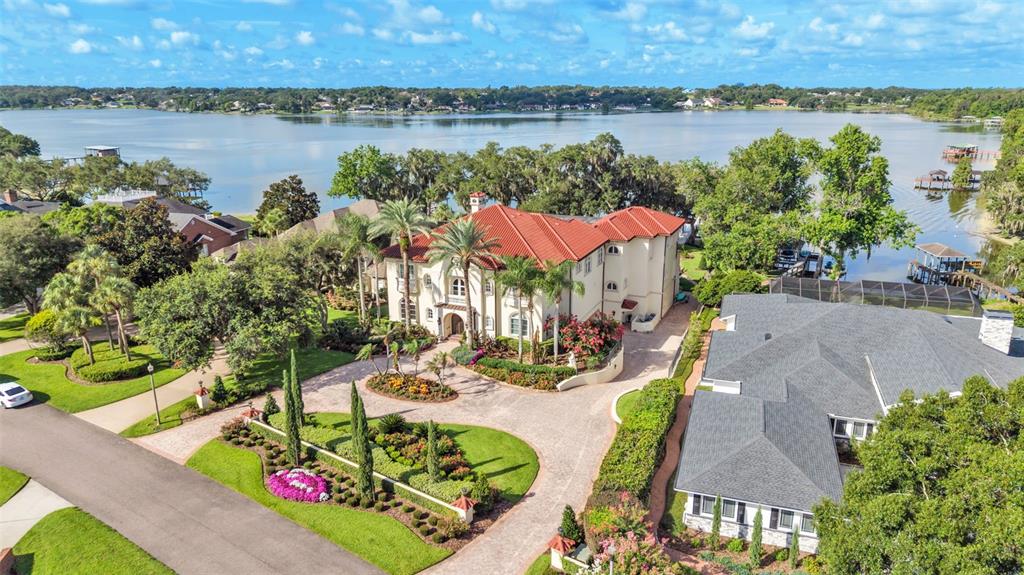 An aerial view shows a large Mediterranean-style house with a red tile roof and driveway — 5119 LAKE IN THE WOODS BOULEVARD, LAKELAND, FL