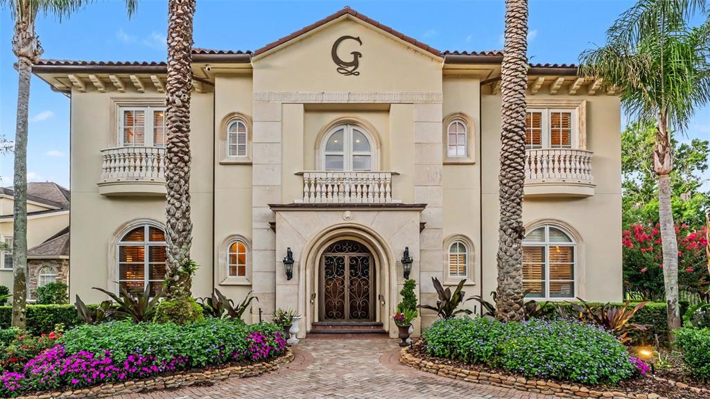 The exterior of a two-story Mediterranean-style house features a stone facade and palm trees — 5119 LAKE IN THE WOODS BOULEVARD, LAKELAND, FL