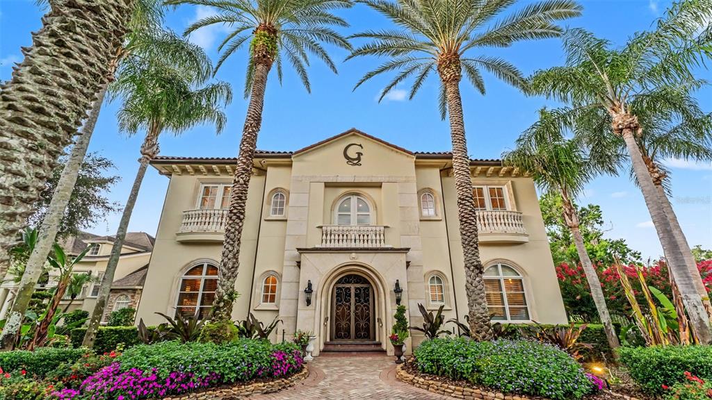 A two-story Mediterranean-style house features a central arched entrance, balconies, and tall palm trees — 5119 LAKE IN THE WOODS BOULEVARD, LAKELAND, FL