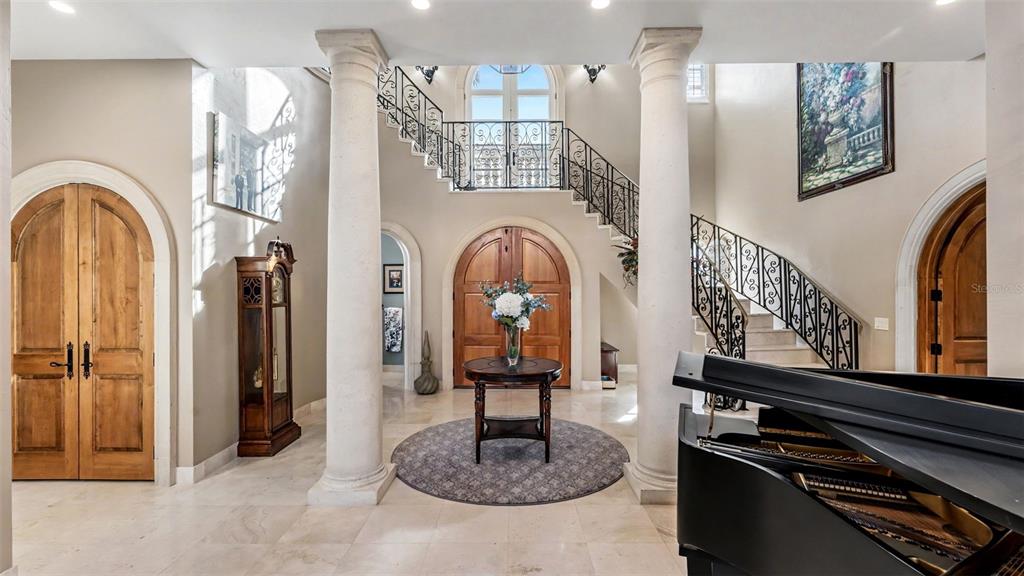 A grand foyer features a dual staircase, marble floors, two large columns, and a piano — 5119 LAKE IN THE WOODS BOULEVARD, LAKELAND, FL