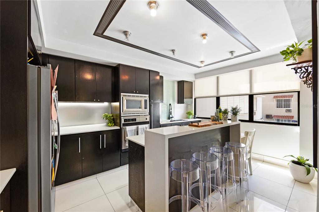 A modern kitchen features dark cabinetry, white countertops, a breakfast bar, and transparent stools — 1504 AVE. ASHFORD, COND. SEA VIEW UNIT 2C, SAN JUAN, PR