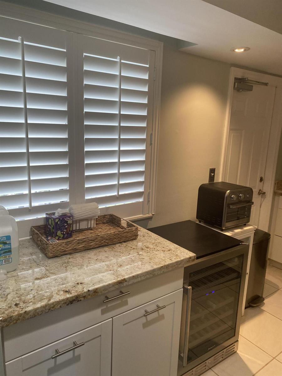 A kitchen counter features a granite top, white cabinets, a wine cooler, and plantation shutters — 1605 S Us Highway 1, Jupiter FL 33477, JUPITER, FL
