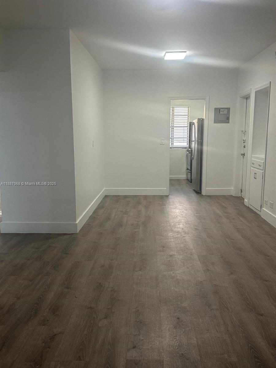 A room with white walls and wood-look flooring leads into a kitchen area — 6805 Abbott Ave # 1, Miami Beach FL 33141, MIAMI BEACH, FL