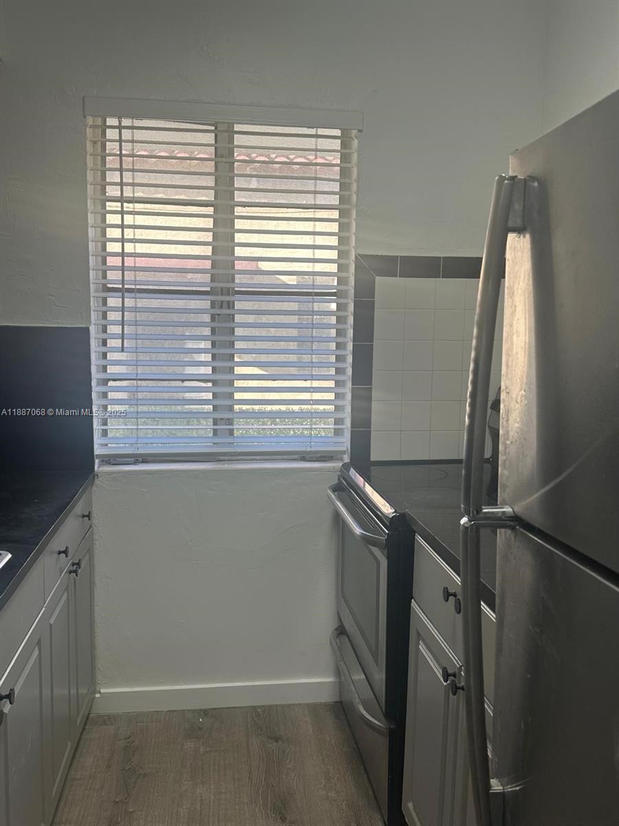 A kitchen features light gray cabinets, black countertops, a stainless steel refrigerator, and a window — 6805 Abbott Ave # 1, Miami Beach FL 33141, MIAMI BEACH, FL