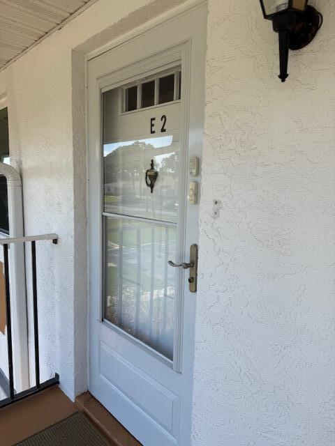 A white front door with a glass panel and the number E2 is set in a stucco wall — 1219 S Lakes End Drive # 2, Fort Pierce FL 34982, FORT PIERCE, FL