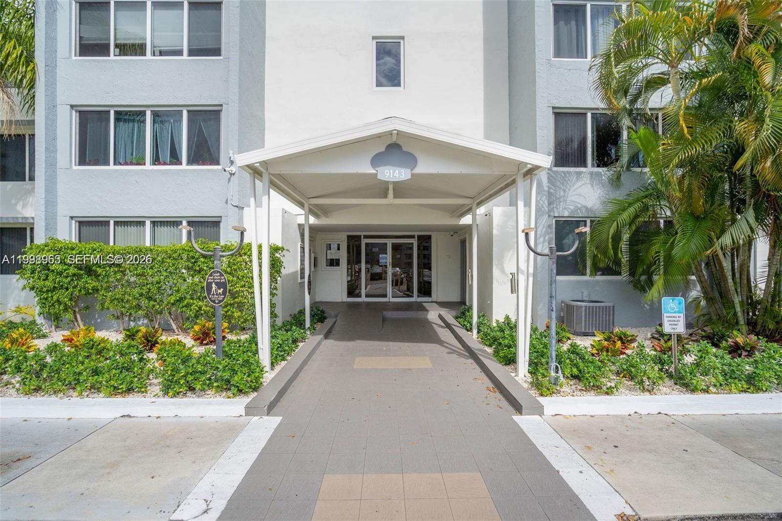 The exterior of a multi-story apartment building features a covered entrance walkway and landscaping — 9143 SW 77th Ave # B105, Miami FL 33156, MIAMI, FL