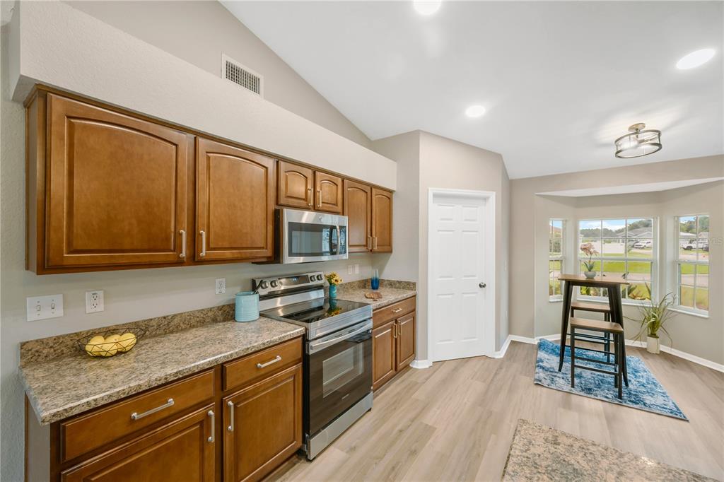 A kitchen features wood cabinets, granite countertops, stainless steel appliances, and an adjacent dining nook — 7811 PRINCETON MANOR CIRCLE, LAKELAND, FL