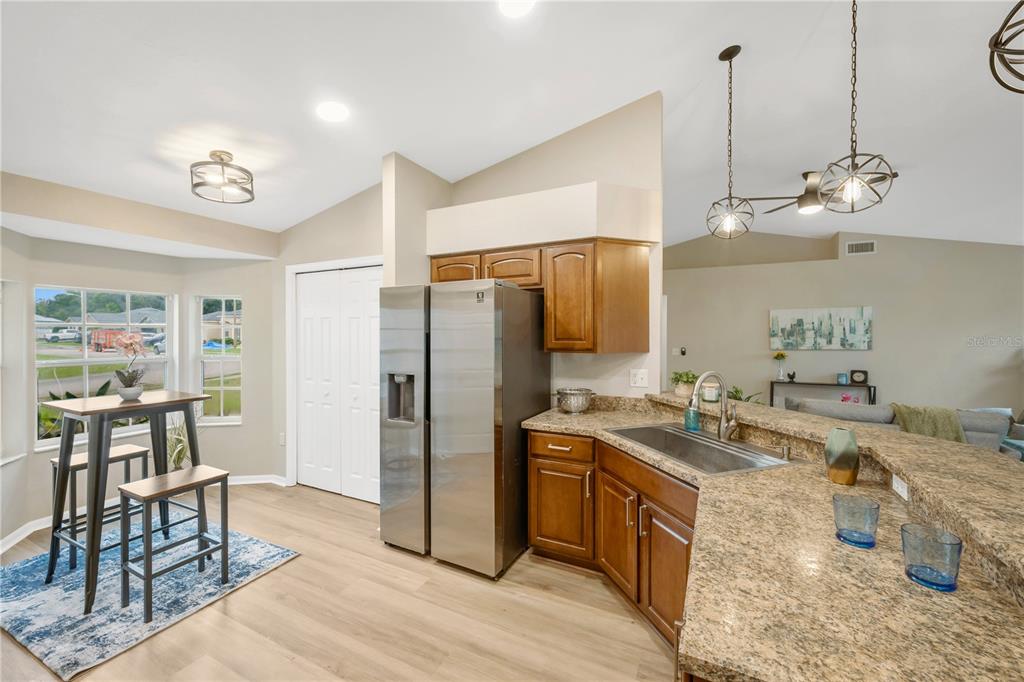 A kitchen with wood cabinets, granite countertops, stainless steel appliances, and a small dining area — 7811 PRINCETON MANOR CIRCLE, LAKELAND, FL