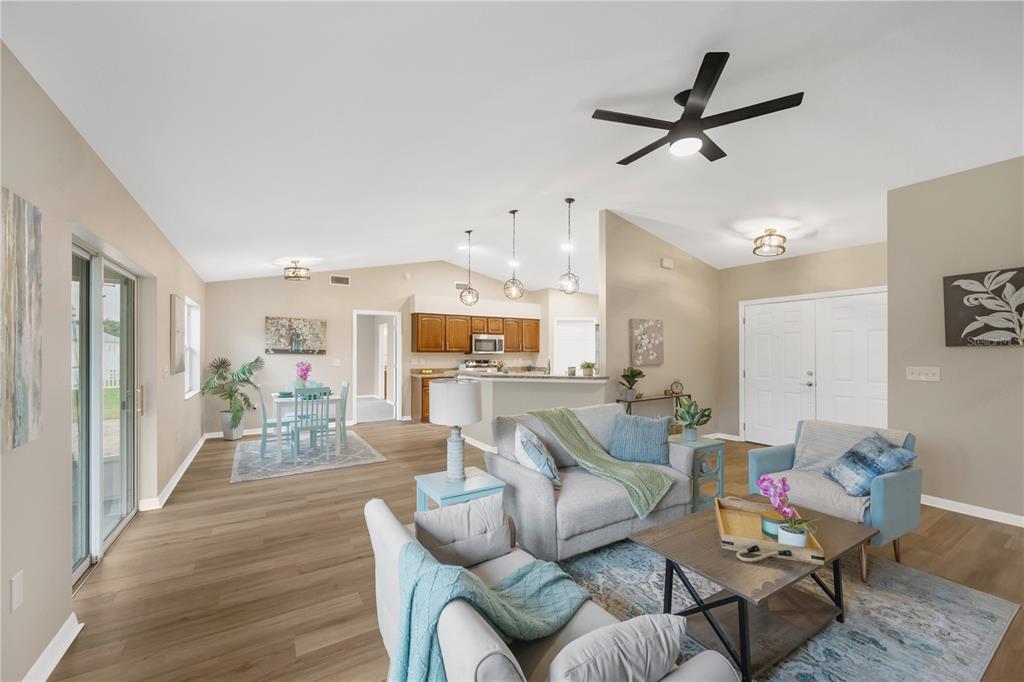 An open-concept living and dining area features light wood flooring, neutral walls, and a kitchen — 7811 PRINCETON MANOR CIRCLE, LAKELAND, FL