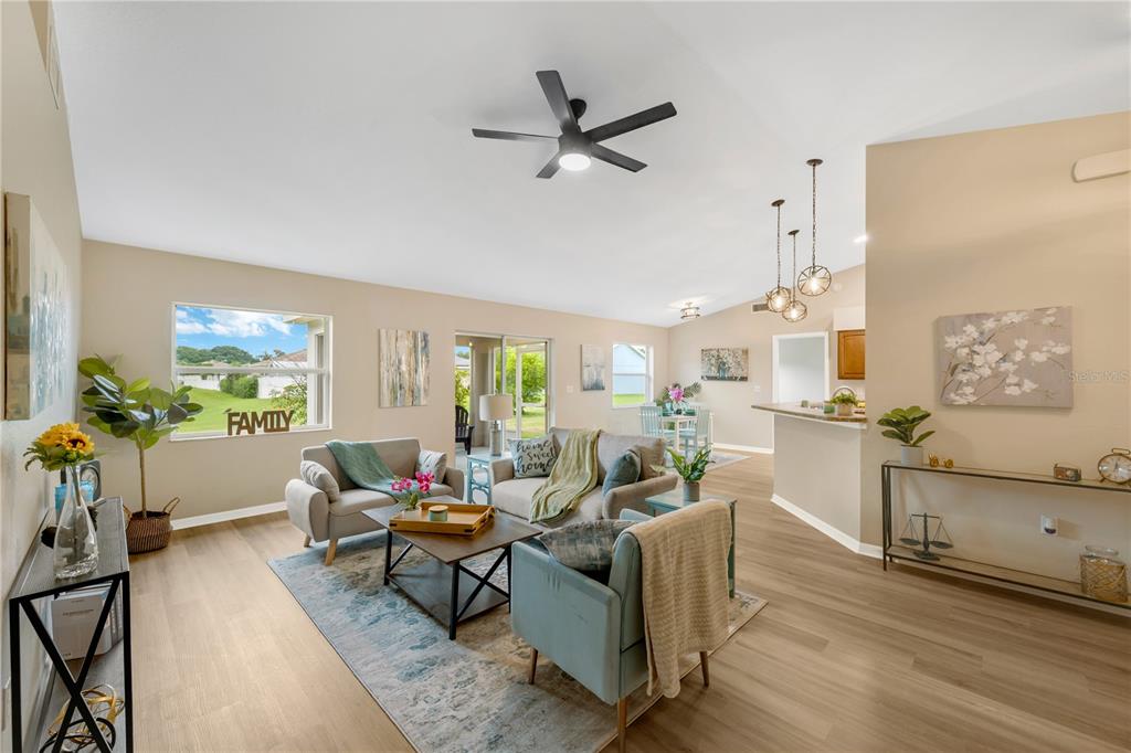 A bright living room features light wood flooring, a ceiling fan, and an open kitchen — 7811 PRINCETON MANOR CIRCLE, LAKELAND, FL
