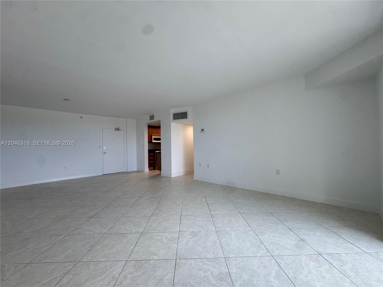 An empty room with white walls and light-colored tile flooring leads to a small kitchen — 10275 Collins Ave # 318, Bal Harbour FL 33154, BAL HARBOUR, FL