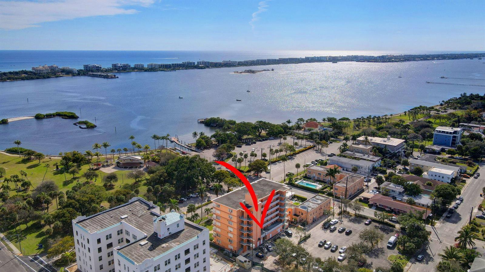 An aerial view shows a multi-story orange apartment building near a waterfront park and bay — 15 S Golfview Road # 204, FL 33460, FL