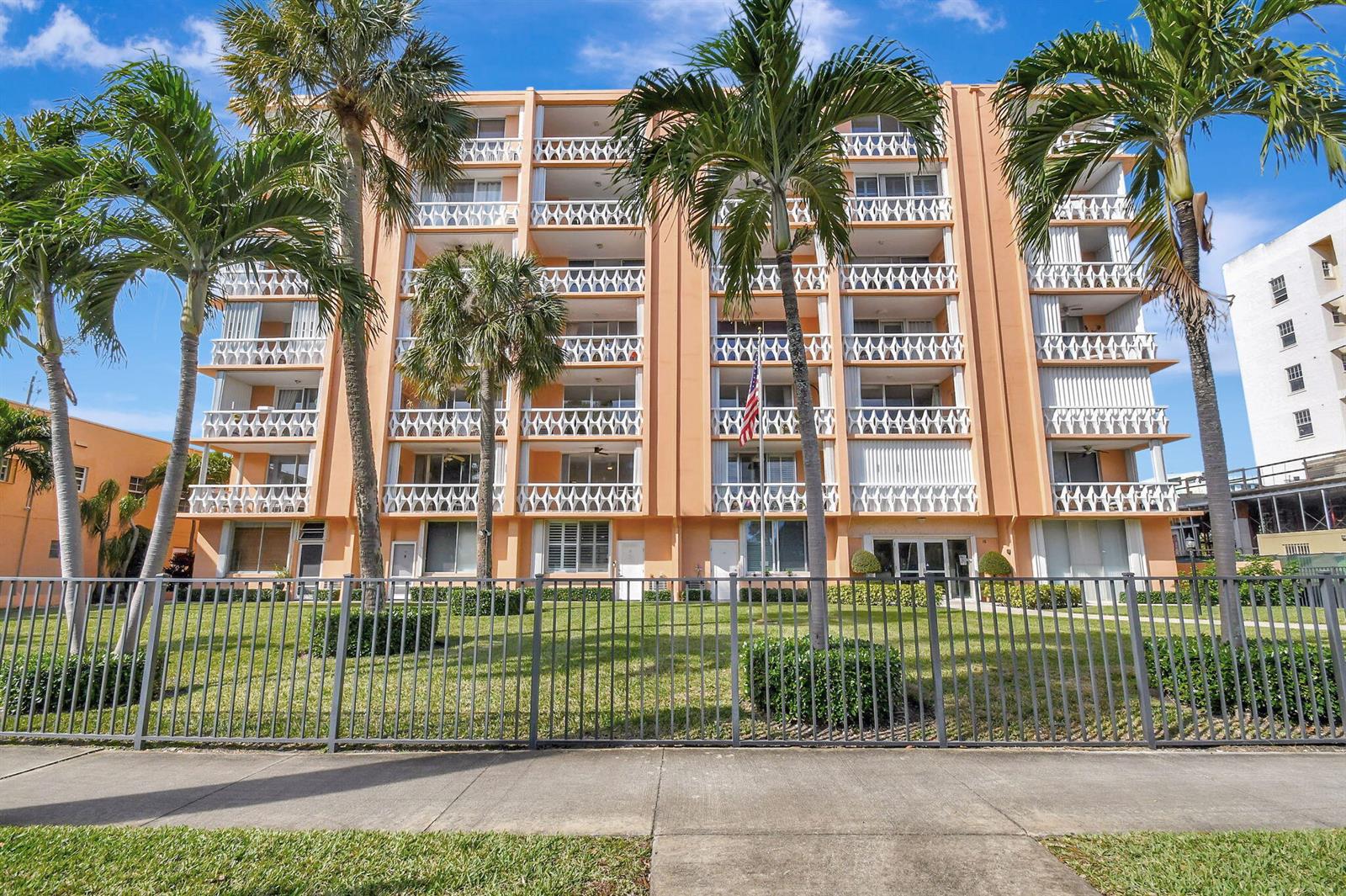 A multi-story peach-colored apartment building with balconies stands behind a metal fence and palm trees — 15 S Golfview Road # 204, FL 33460, FL