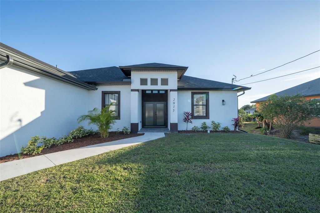 A single-story house with a white stucco exterior, dark trim, and a central entryway — 2915 5TH STREET SW, LEHIGH ACRES, FL