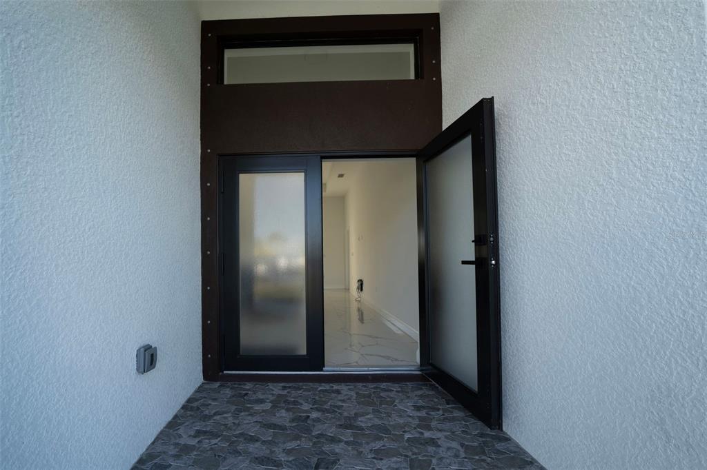 A modern front entrance features a dark-framed glass door with a transom window and stone flooring — 2915 5TH STREET SW, LEHIGH ACRES, FL