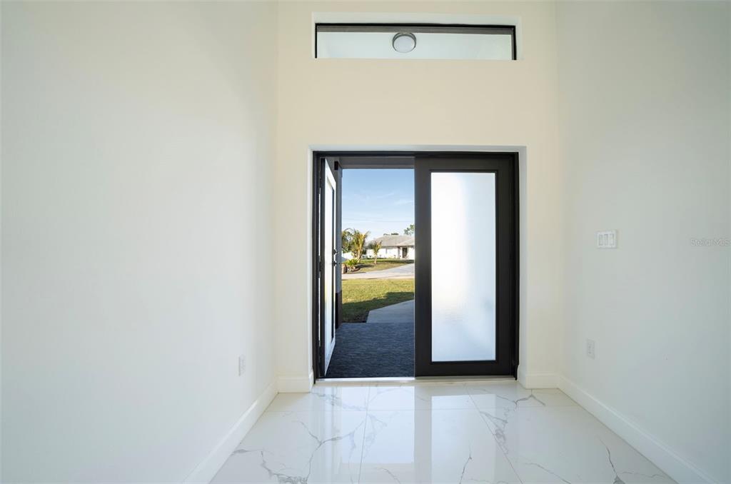 An entryway with white marble-look tile floors leads to an open front door — 2915 5TH STREET SW, LEHIGH ACRES, FL